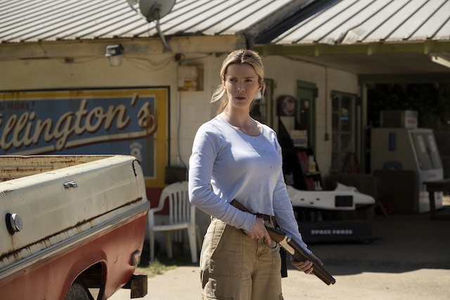 銃を手に、ガソリンスタンドで周囲を警戒するクリスタル 映画『ザ・ハント』で、ベティ・ギルピン演じるクリスタルがガソリンスタンドの前で銃を持ち、周囲を警戒している